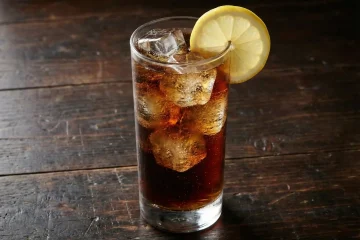 Gotowy drink brandy z colą w wysokiej szklance z lodem i cytryną.